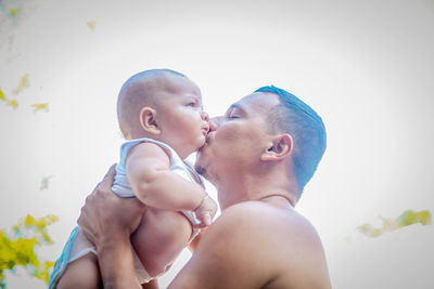 Father kissing son against clear sky