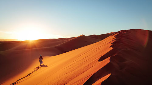 Silhouette man on sand dune in desert against clear sky