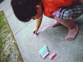 High angle view of boy writing with chalk on footpath