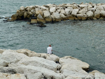 Rear view of woman standing on rock by sea