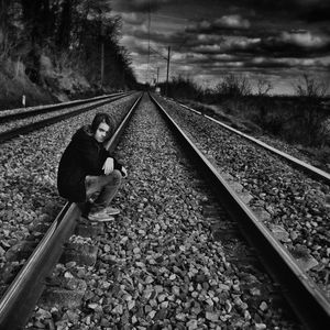 Boy looking away while sitting on railroad track against sky