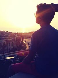 Midsection of man sitting in city against sky during sunset