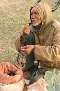 Senior vendor selling food while sitting on grassy field