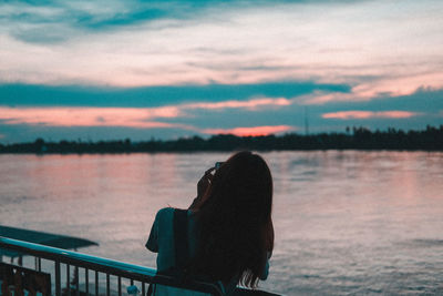 Rear view of man looking at lake against sunset sky