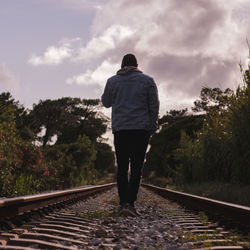 Rear view of man standing on railroad tracks against sky
