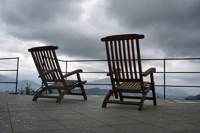 Wooden deck chairs against cloudy sky