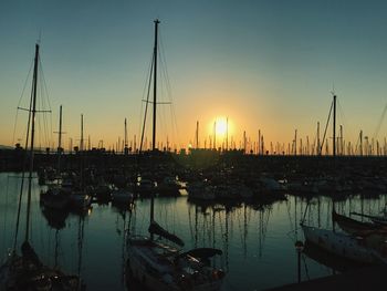 Sailboats moored in harbor at sunset