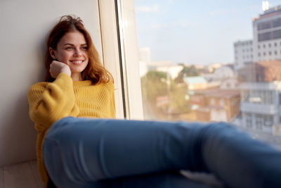 Portrait of smiling woman sitting on window