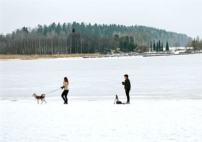 Man with camera by woman holding dog at beach during winter