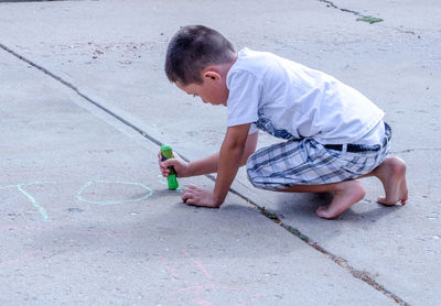 Young boy writing letters on the cement with sidewalk chalk