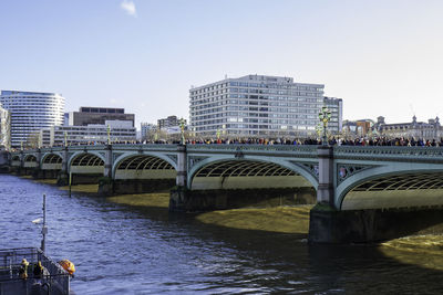 Bridge over river by buildings against clear sky