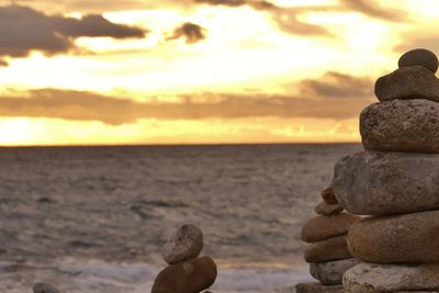 Stack of pebbles on beach against sky during sunset