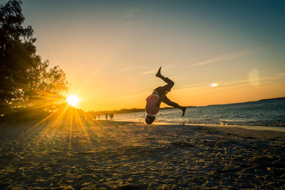 Man performing stunt at beach during sunset