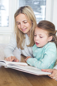 Girl with mother reading book at home