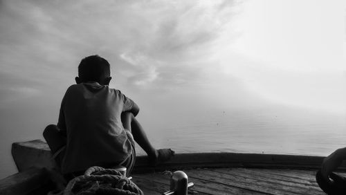 Rear view of man sitting by sea against sky