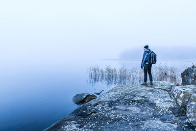 A lone hiker admires the beauty of nature reflected in a tranquil lake, surrounded by misty skies 