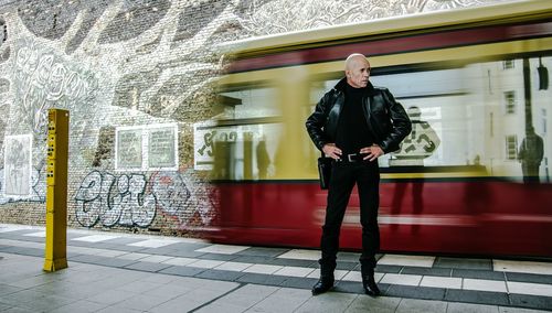 Man standing with hands on hip against blurred motion of tramway