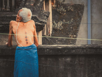 Rear view of shirtless man standing by staircase