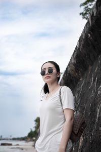 Young woman wearing sunglasses while standing by stone wall at beach