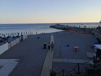 People on beach against clear sky during sunset