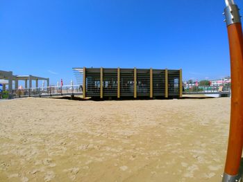 Beach by buildings against clear blue sky