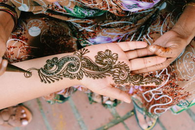 Midsection of woman drawing henna tattoo on hand