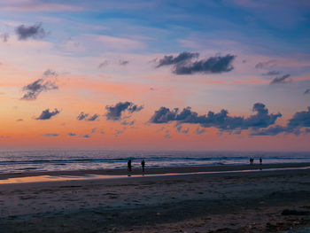 Silhouette people on beach against sky during sunset