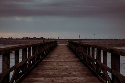 Wooden footbridge over sea against sky