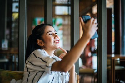 Portrait of smiling young woman photographing through window