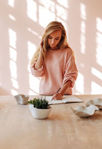 Young woman writing in book on table at home