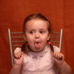 Cute girl sticking out tongue while holding pigtails against orange wall