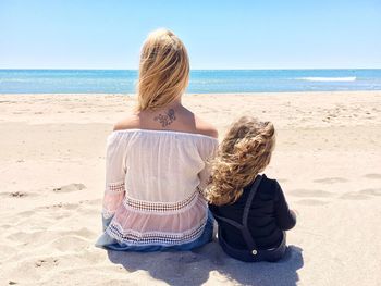 Rear view of woman sitting with daughter at sandy beach