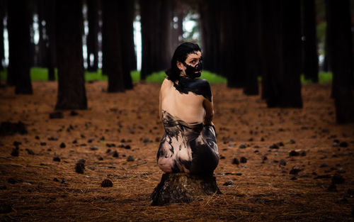 Portrait of naked woman covered with paint while sitting in forest