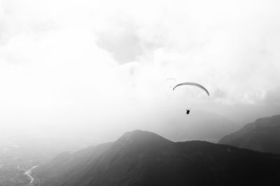 Person paragliding over mountain against cloudy sky