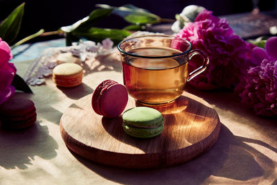 Herbal tea and macarons dessert for brunch outside. blooming pink peony flowers, hard shadows. 