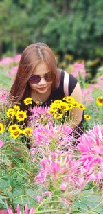 Young woman with pink flower standing against yellow flowering plants