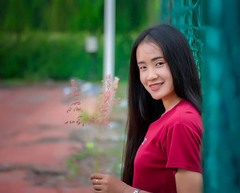 Portrait of smiling woman standing by fence