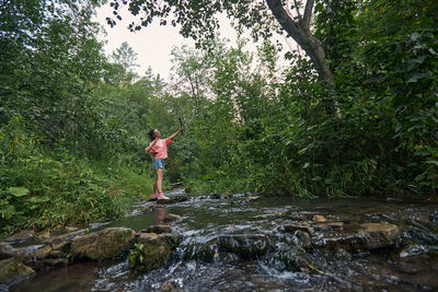 Man standing on rock by river against trees