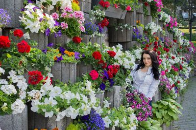 Beautiful woman standing amidst various flower pots on wall at park