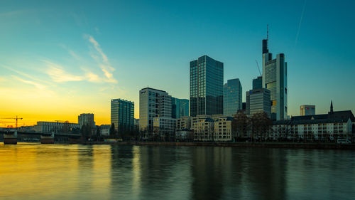 River by buildings against sky during sunset