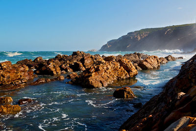 Rock formations on shore against clear sky