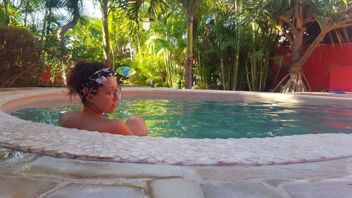 Rear view of woman sitting in hot tub against trees