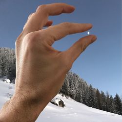 Close-up of hand holding snow against sky