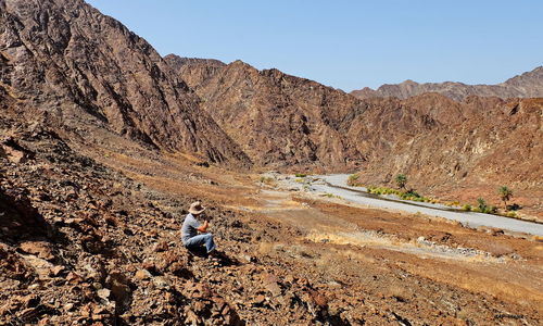 Full length of man sitting on rock against sky