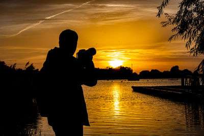 Silhouette man standing by lake during sunset