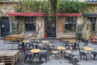 Empty chairs and tables at sidewalk cafe against buildings in city