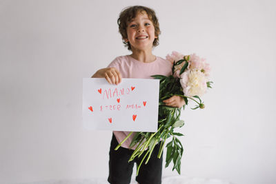 Cheerful happy child with peonys bouquet and a card for mom in ukrainian language.