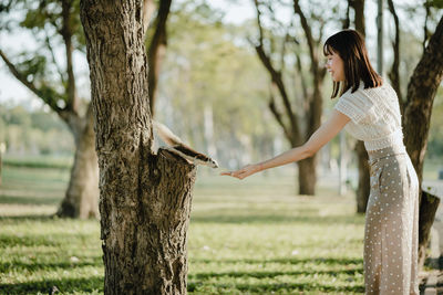 Woman standing by tree trunk on field