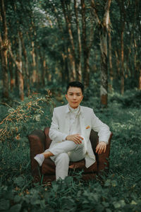 Portrait of young man sitting on chair at forest