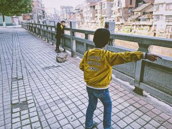 Rear view of boy standing by railing in city